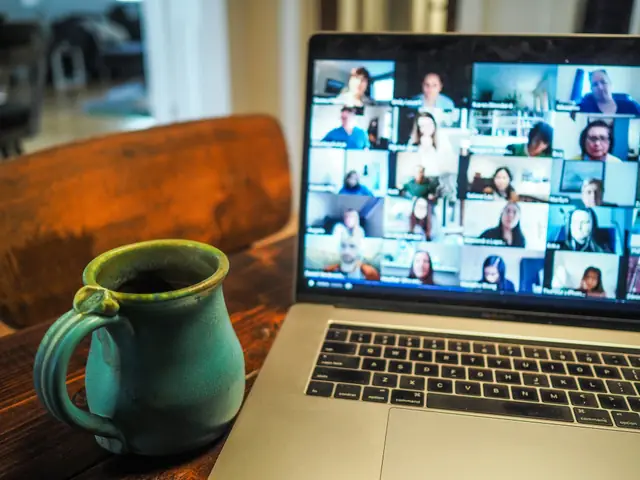 A laptop showing a video call grid next to a coffee mug